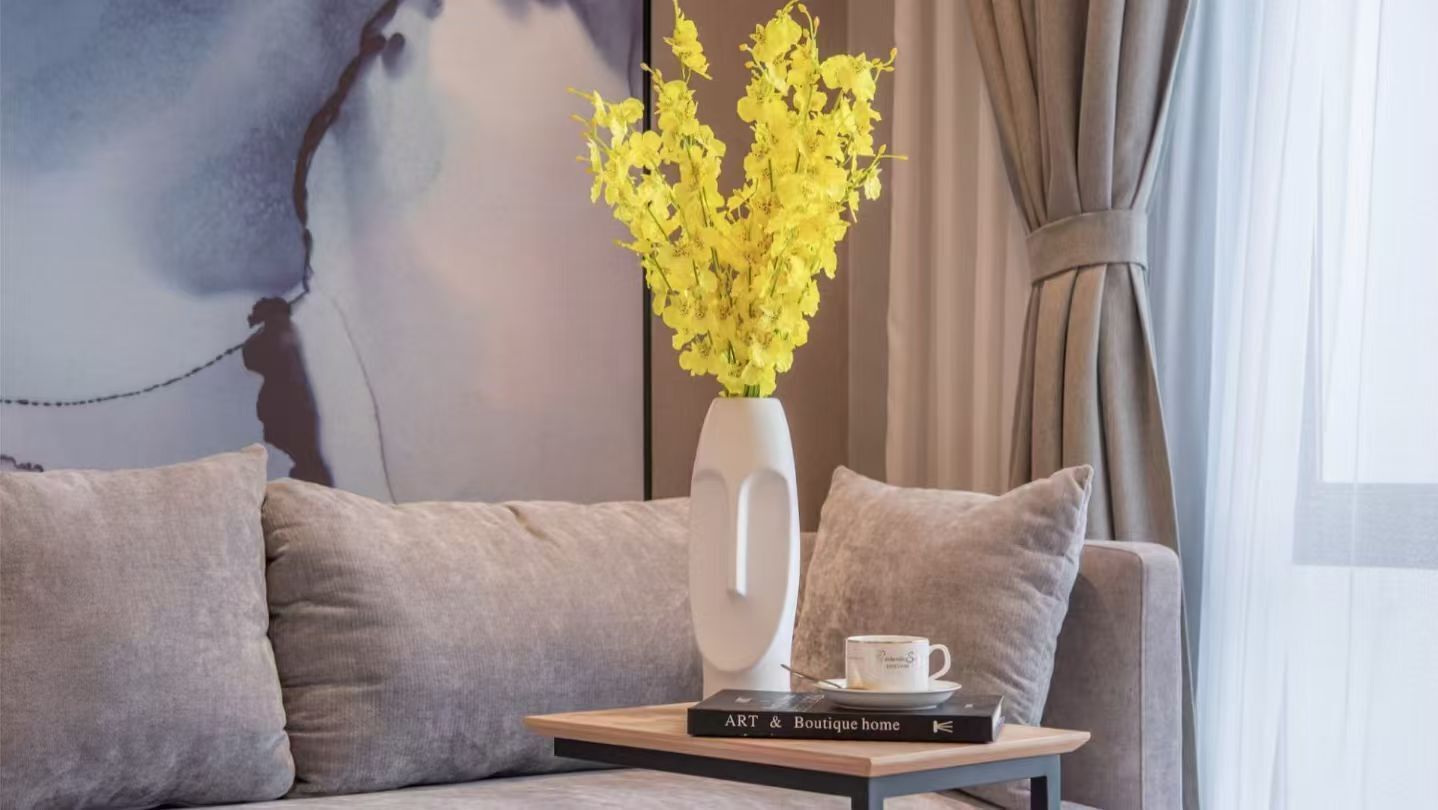 Un salon moderne avec un canapé, une petite table sur laquelle repose un livre, un vase rempli de fleurs jaunes et une tasse.