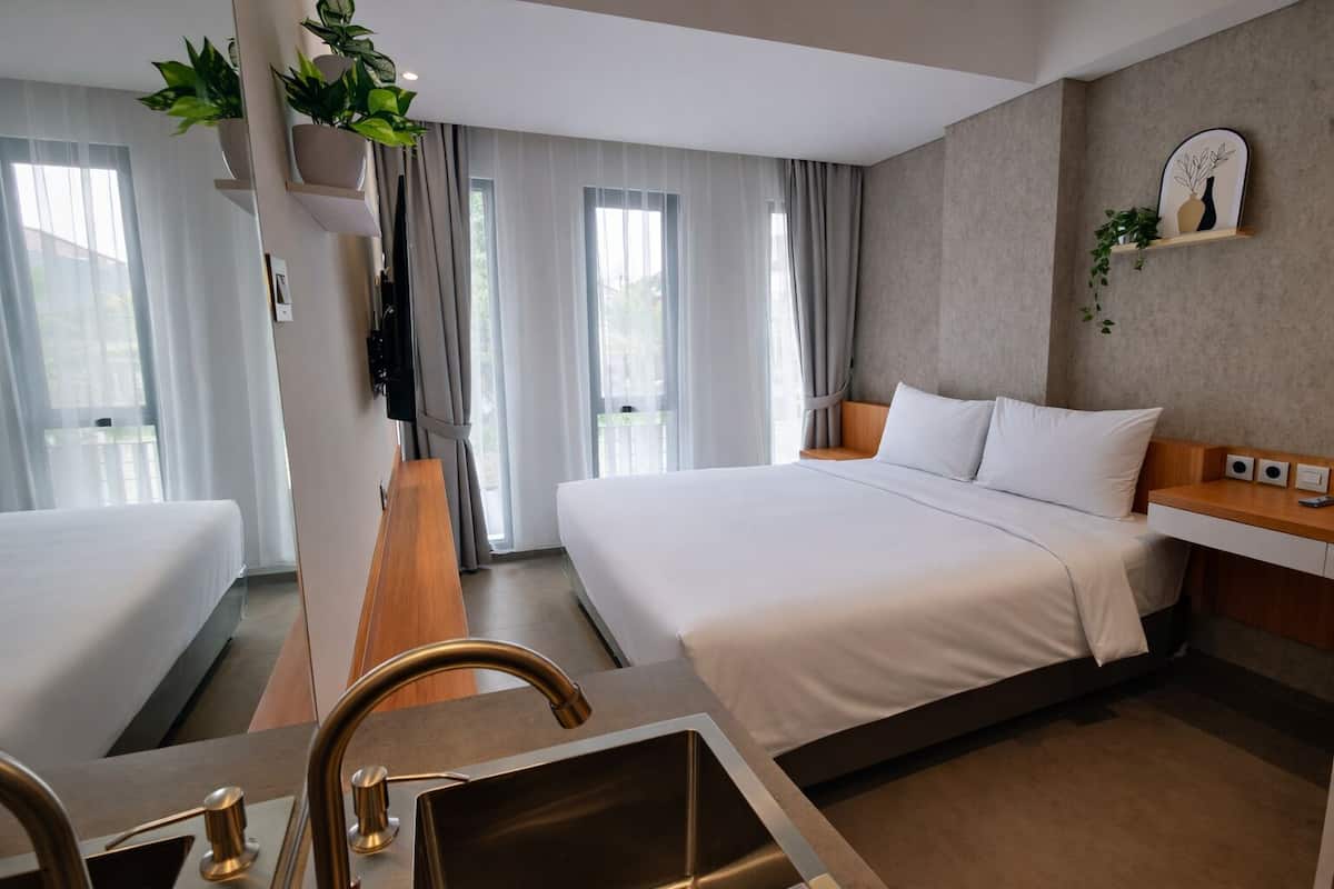 Une chambre d’hôtel avec un grand lit, un bureau en bois, un lavabo intégré et une vue sur l’extérieur grâce à de grandes fenêtres.