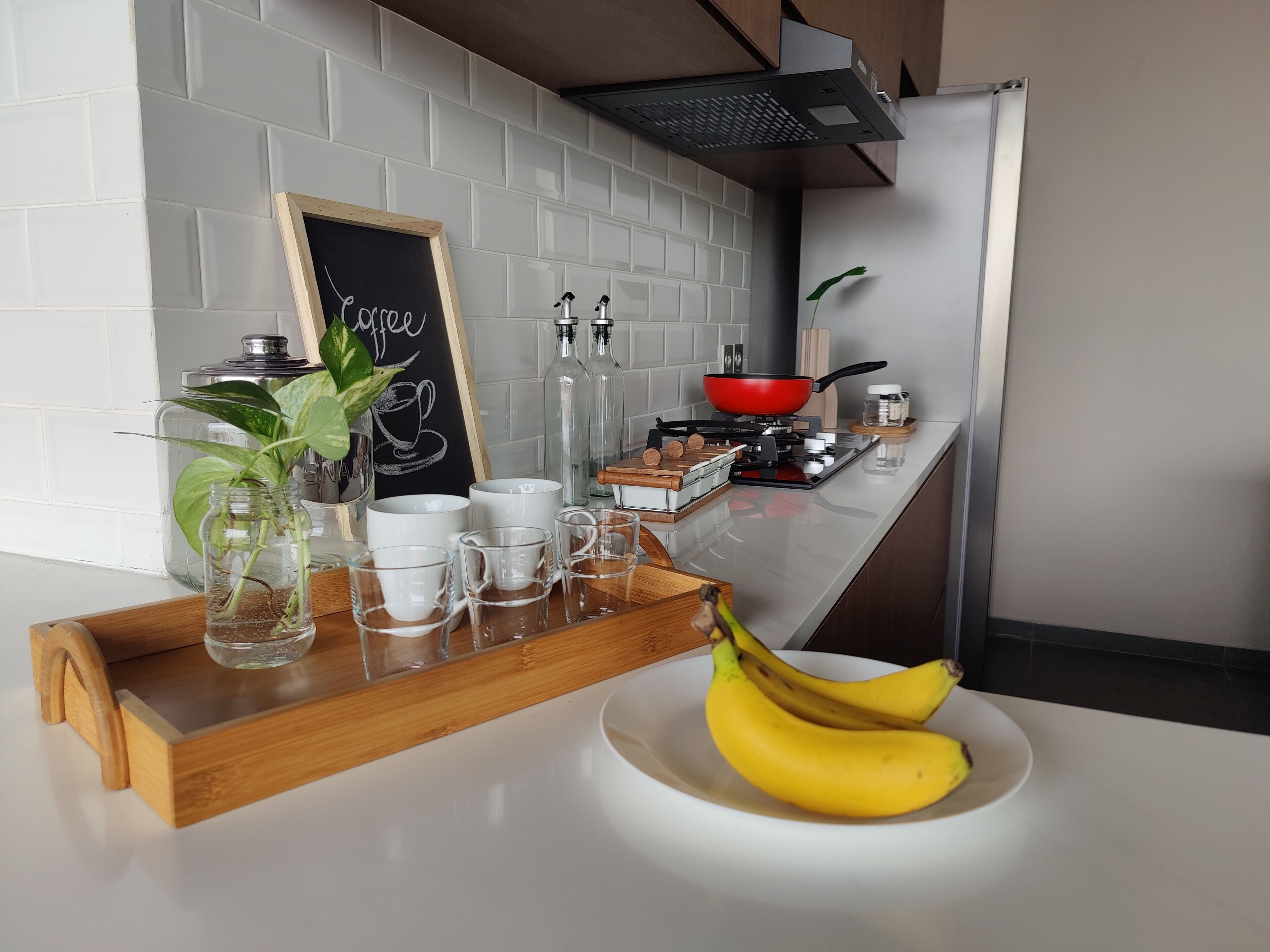 Een aanrecht met een dienblad waarop mokken staan, een bordje met de tekst 'koffie' en een schaal met bananen.