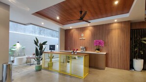 Un área de recepción moderna con techo de madera, ventilador de techo, mostrador de recepción con máquina de café y un separador amarillo.