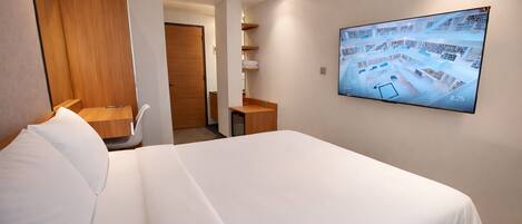 Een hotelkamer met een bed, een houten garderobe, een bureau, een stoel, een televisie aan de muur en een deur die naar een andere kamer leidt.