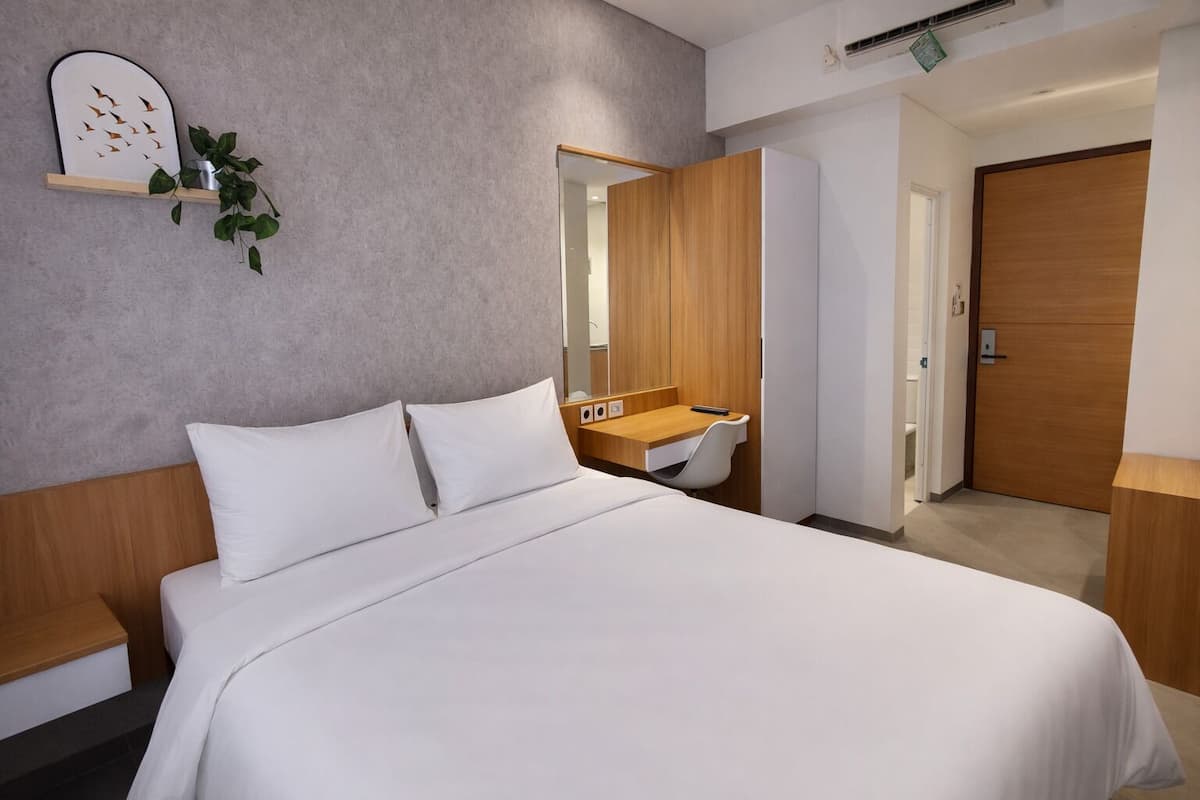 Une chambre d’hôtel moderne avec un grand lit, un bureau en bois, un miroir et une plante posée sur une étagère.