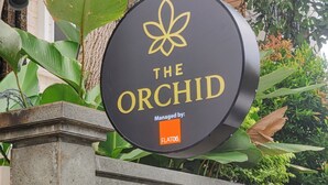 Un letrero que dice 'The Orchid', administrado por FLAT06, rodeado de follaje.