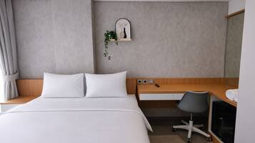 Una camera d'albergo con un letto, una scrivania, una sedia, una piccola pianta e uno specchio.