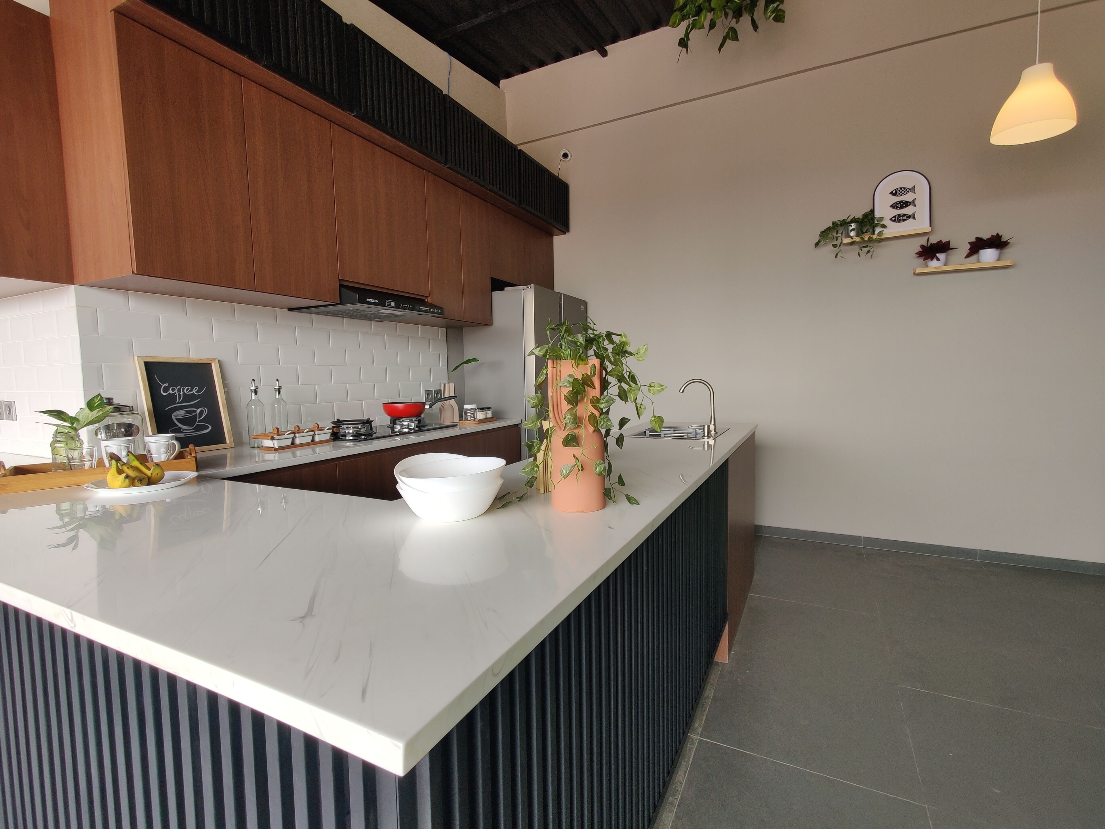 Une cuisine moderne avec un plan de travail en marbre blanc, des armoires en bois et un pare-feu noir. On y trouve une cuisinière, un évier et divers ustensiles de cuisine sur le plan de travail.