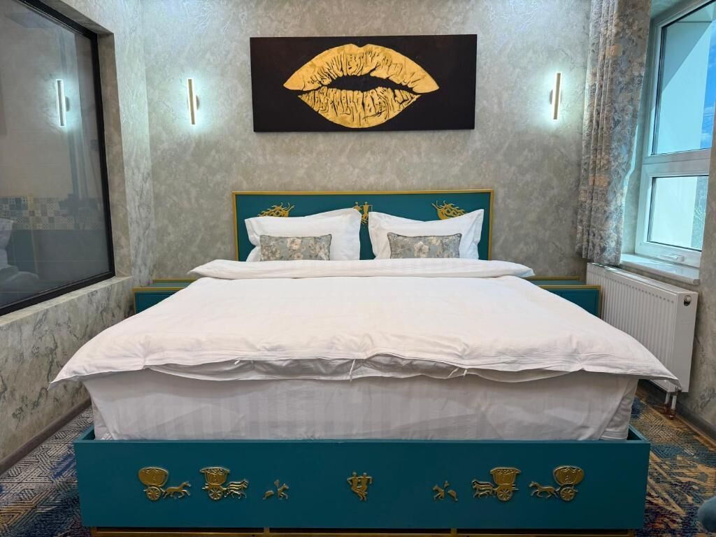 A bedroom with a bed, a large wall art of lips, and a window.