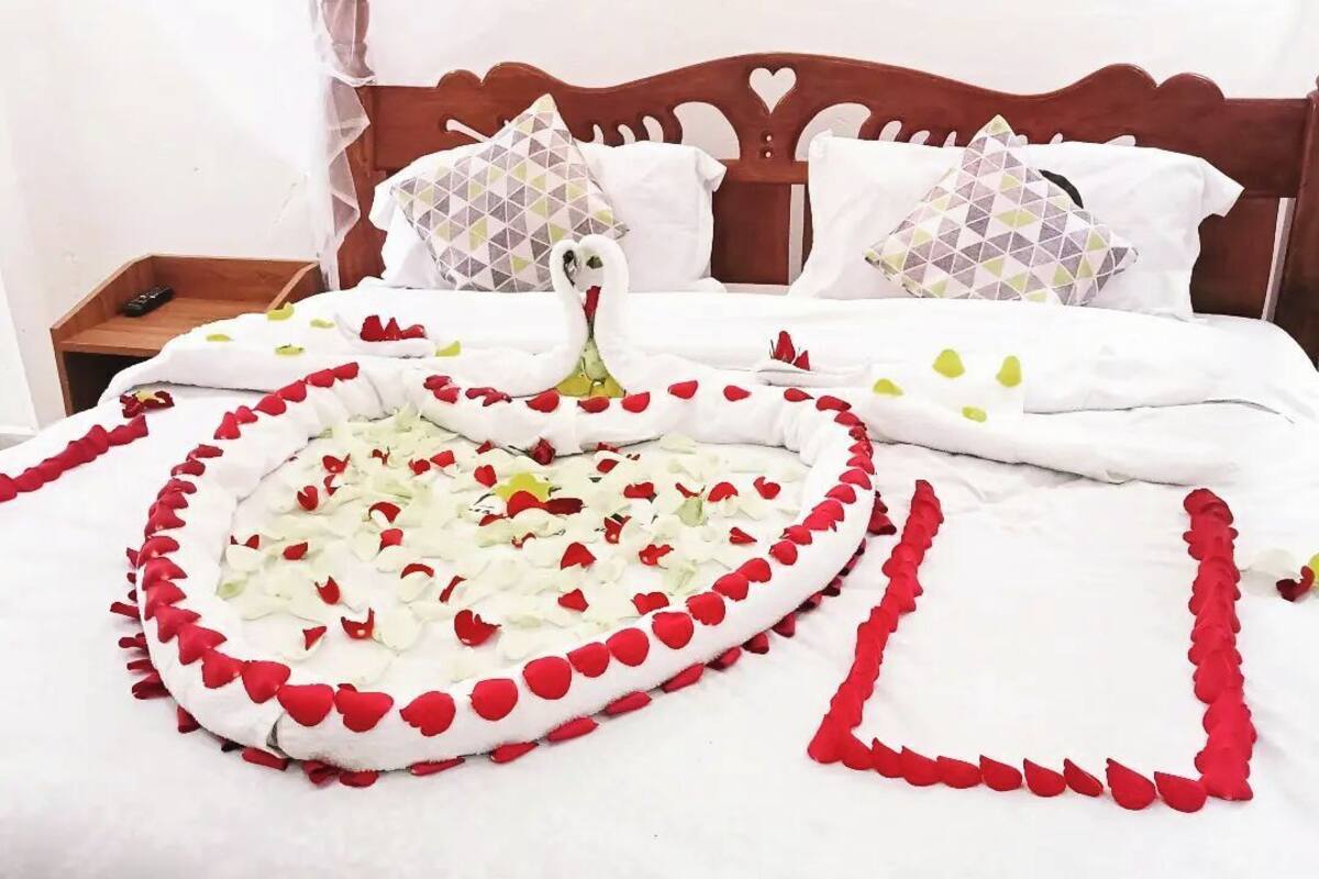 A neatly made bed with a heart-shaped arrangement of rose petals and a swan decoration.