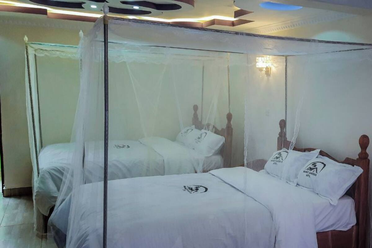 A room with two beds, each with a canopy. The beds have white linens and pillows with logos. There is a mirror on the wall and a light fixture above the beds.