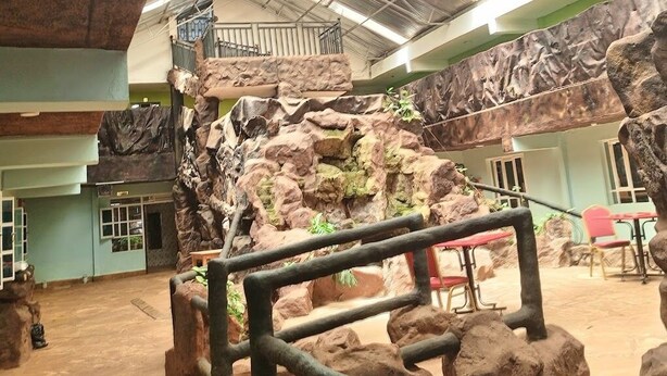 Un espacio interior con techo alto, un paisaje artificial rocoso y una barandilla de metal.
