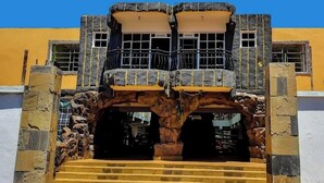 Un edificio con fachada amarilla, arco de piedra y un balcón con barandilla de metal.