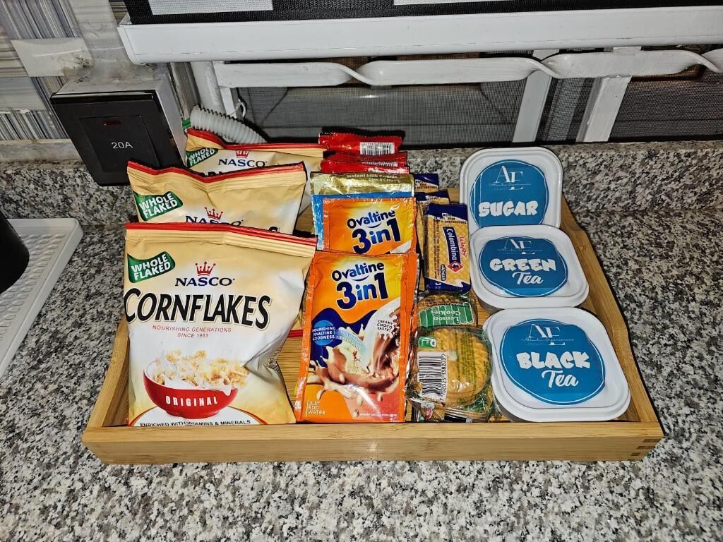 Egy fa tál, melyben különféle élelmiszerek találhatók, például kukoricapelyhek, narancslé, cukor, tea és más rágcsálnivalók.