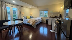Habitación de hotel compacta con cama, una pequeña mesa de comedor, una silla, kitchenette y ventana con vistas a zonas verdes.