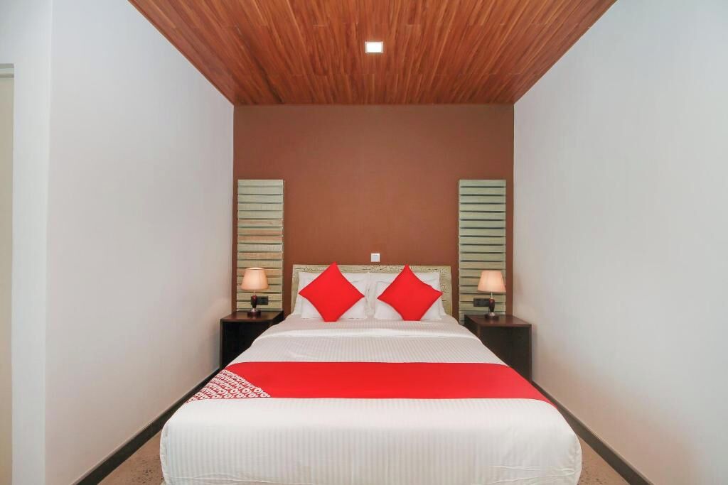 Une chambre d’hôtel avec un lit, deux tables de chevet, un plaid rouge et un plafond en bois.
