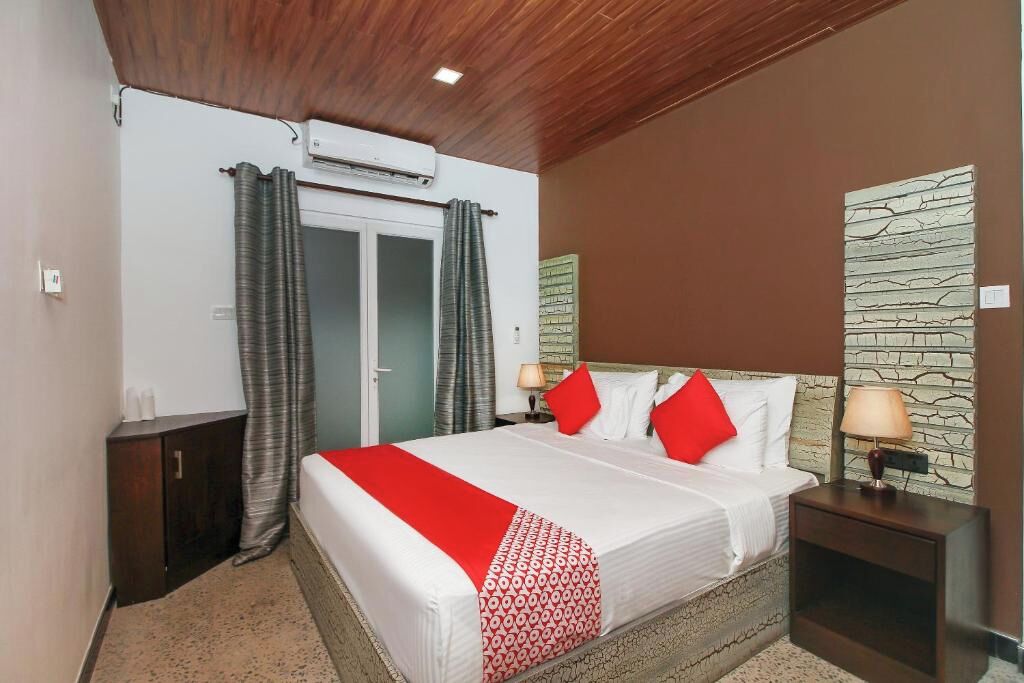 A hotel room with a bed, a nightstand, a wardrobe, a window with curtains, and a wall-mounted air conditioner.