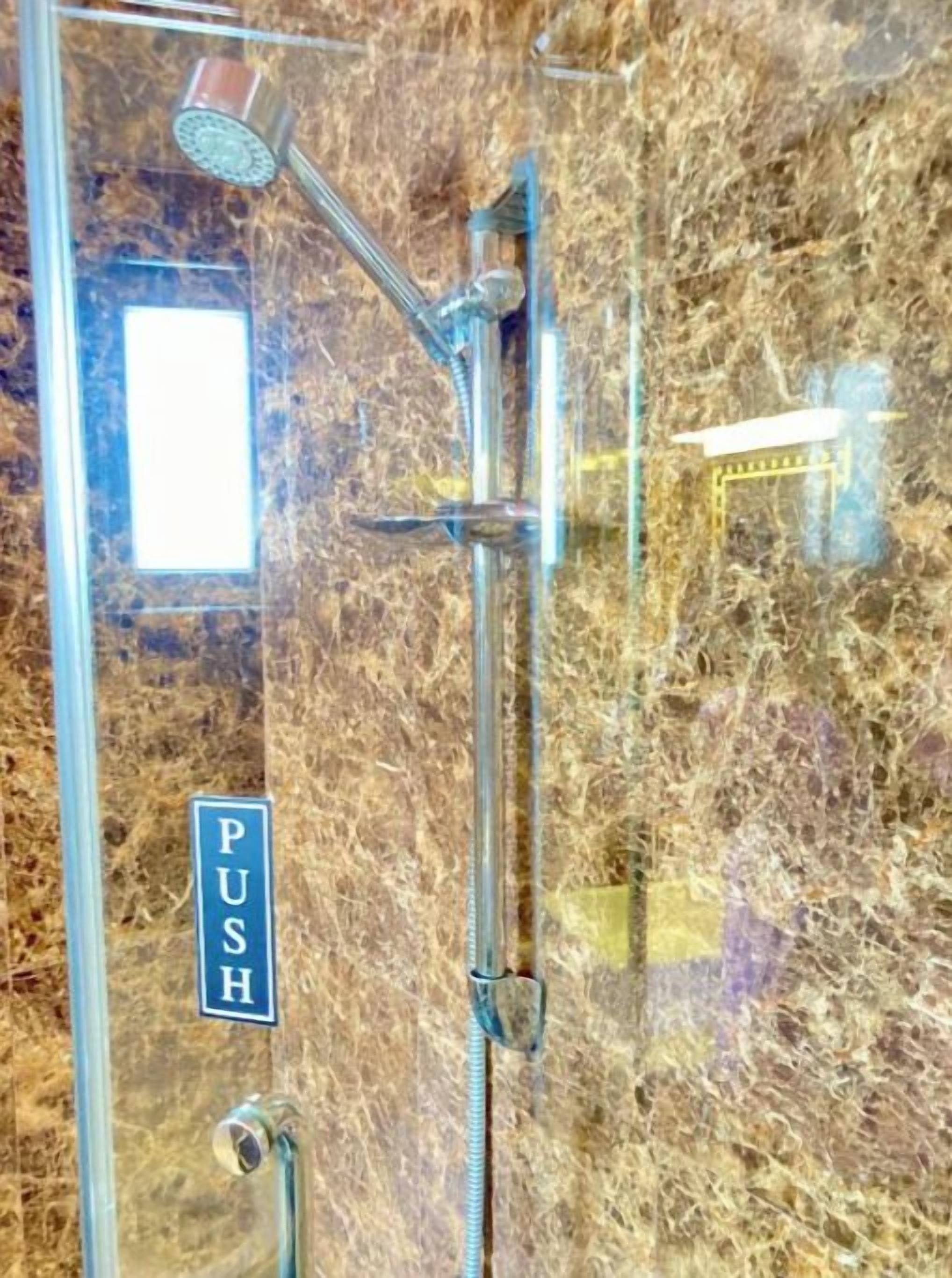A shower with a push button, a glass enclosure, and a marble wall.