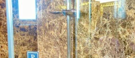 A shower with a push button, a glass enclosure, and a marble wall.