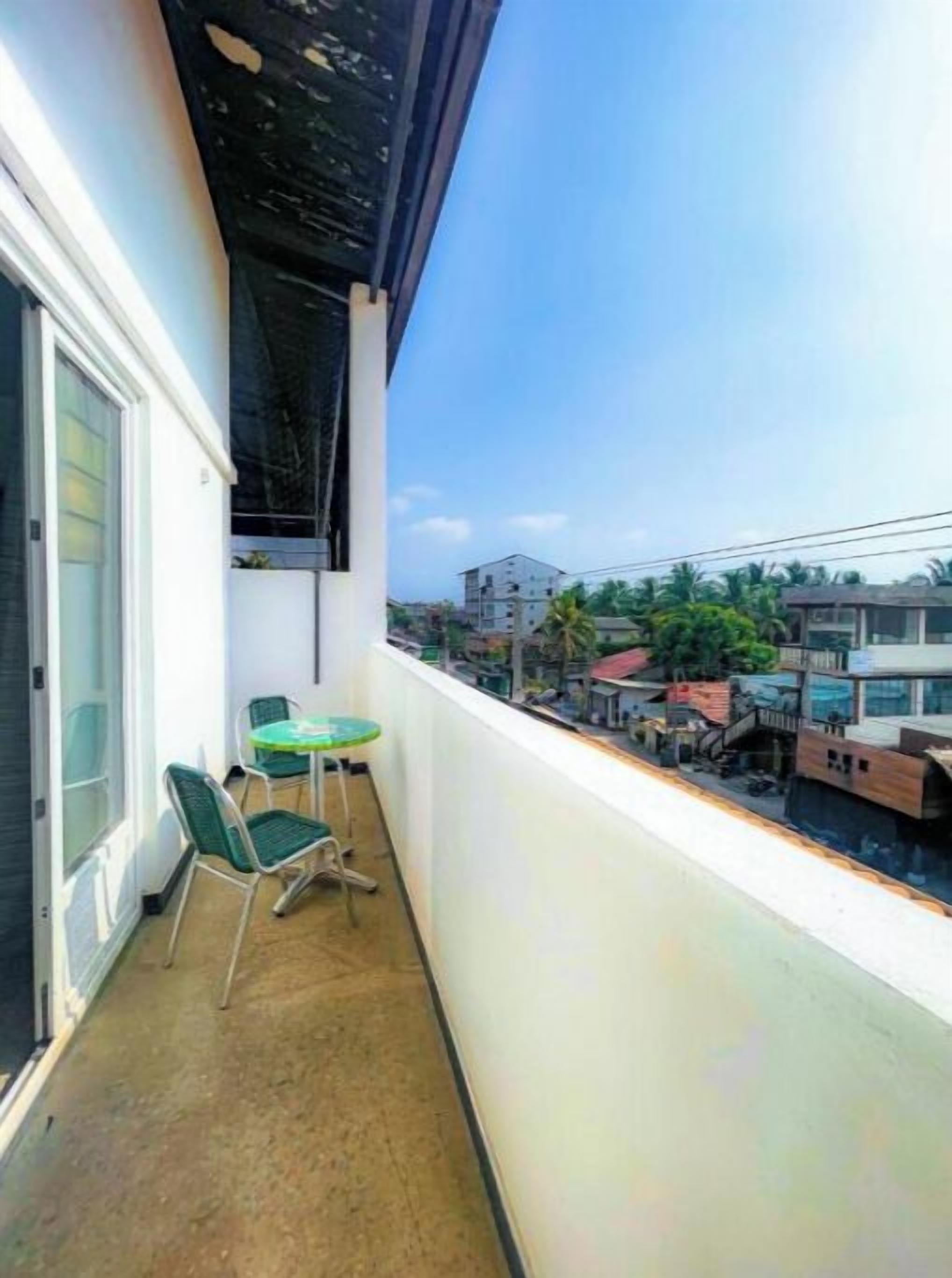 A balcony with a table and chairs, a window, and a view of buildings and palm trees.