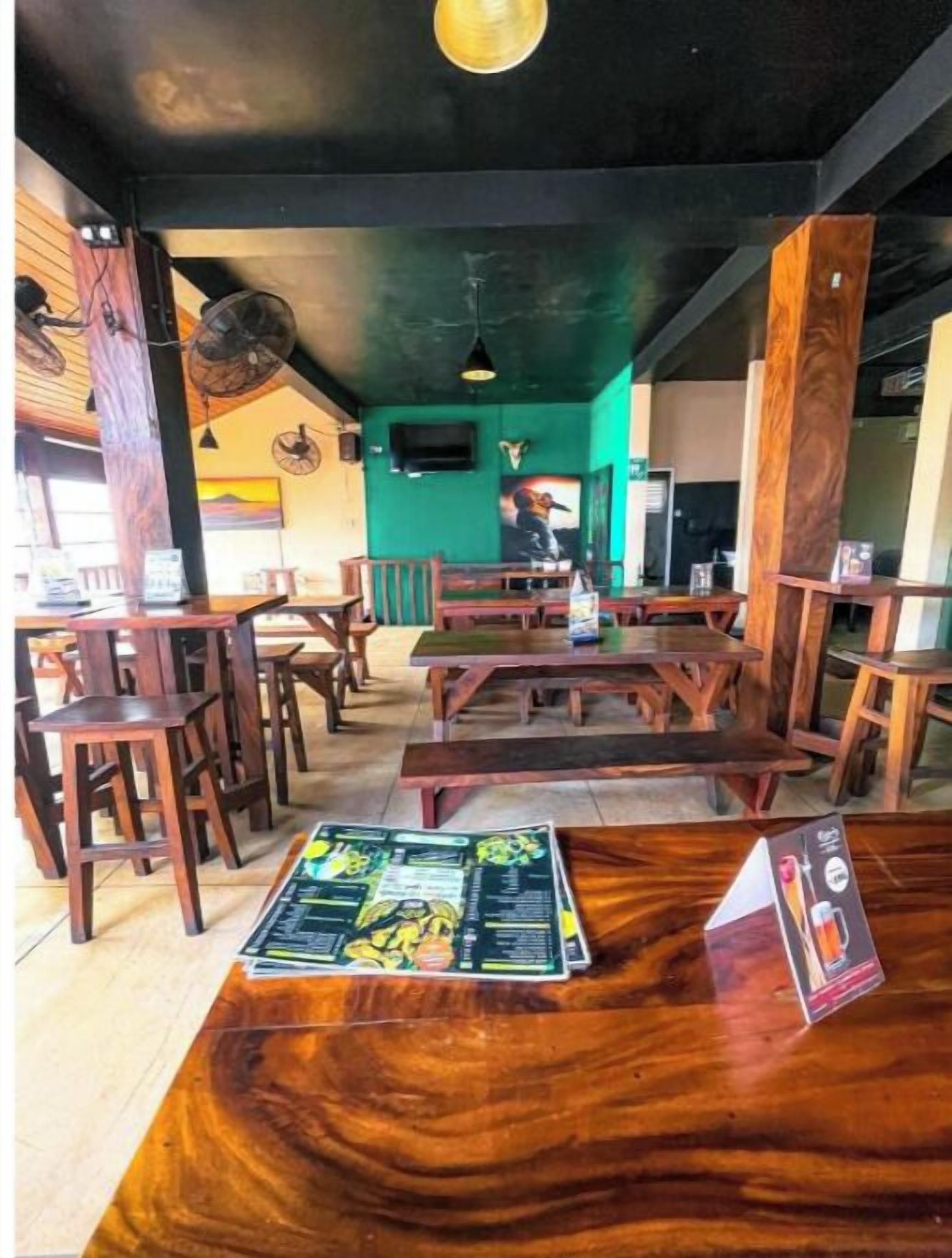 Ein Restaurantinneres mit Holztischen und -stühlen, einer grünen Wand und einem Deckenventilator.