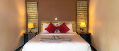A neatly made bed with two red pillows, two bedside lamps, and a small bench at the foot of the bed.
