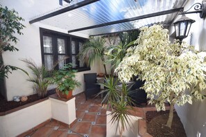 En overdækket terrasse med plantekasser, et bord og stole.