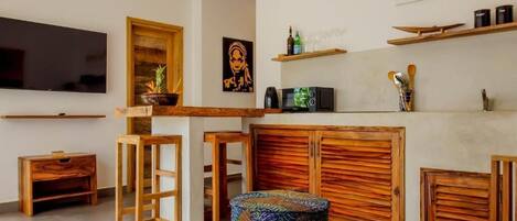 Una sala de estar con un mueble bajo de madera para el televisor, un televisor de pantalla plana, un aparador de madera y un otomano tejido y colorido.