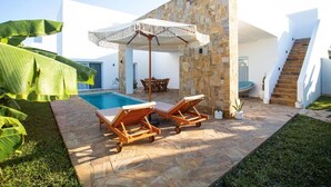 A pool area with lounge chairs and an umbrella, surrounded by stone walls and greenery. - CDM Villas (Kiwengwa)