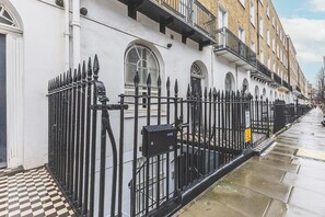 A row of white buildings with black iron fences, a checkered pavement, and a clear sky. - Modern Baker Street Flat with Patio (London)