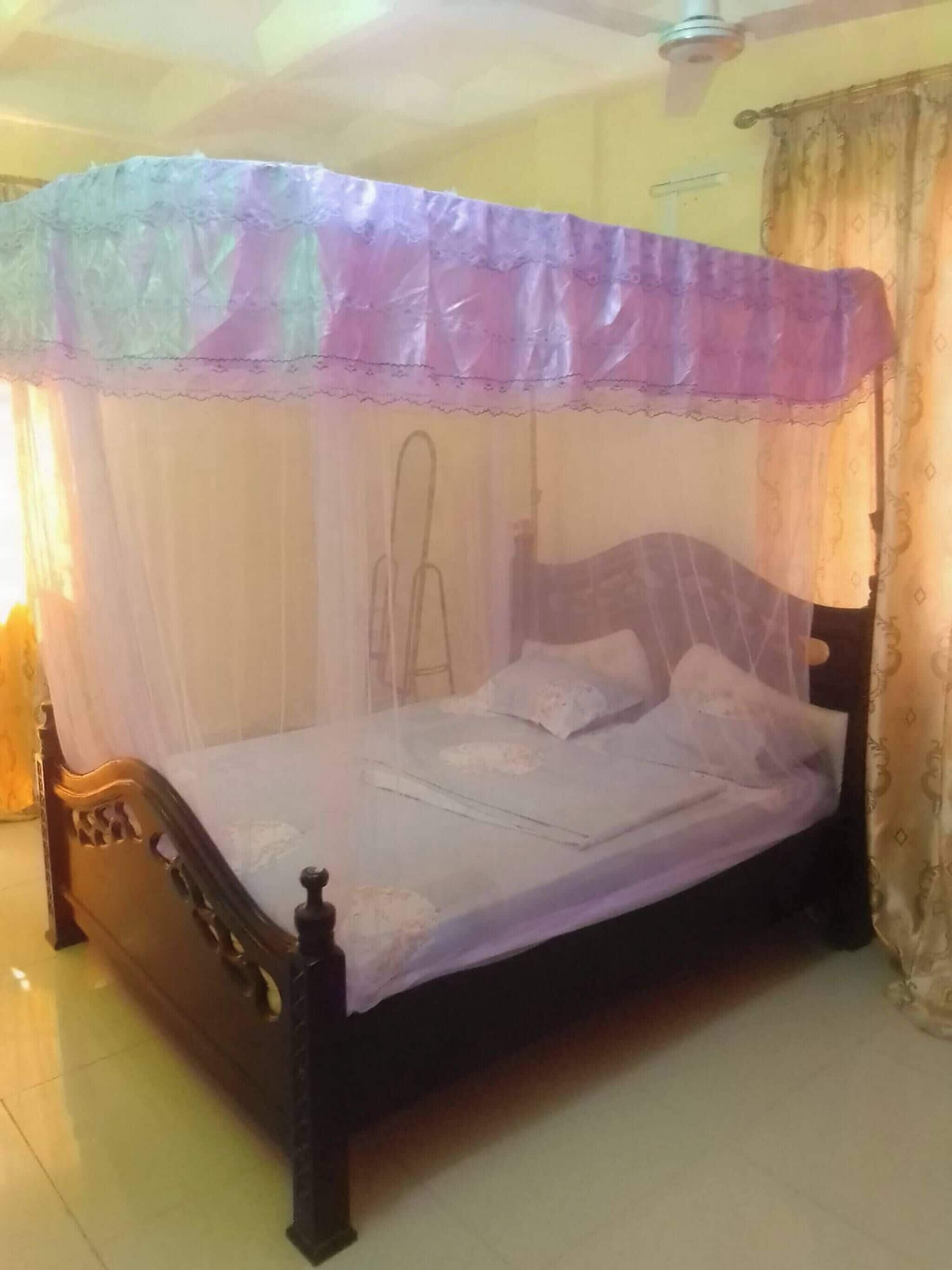 A bed with a canopy, a wooden headboard, and a plain wall.