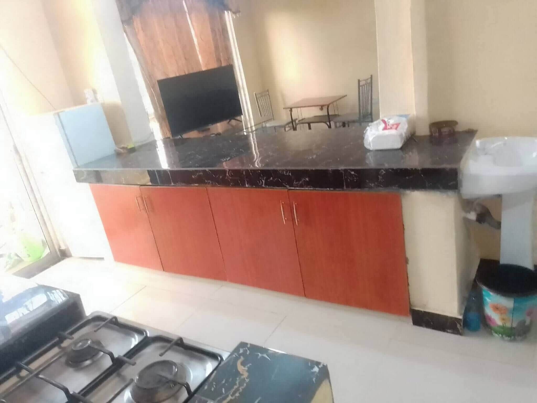 A kitchen with a black countertop, red cabinets, a gas stove, and a sink.