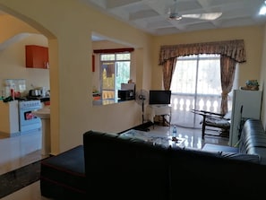 A living room with a sofa, a TV, a fan, and a kitchen area with a stove and sink. - Furnished Flat Apartment Bamburi Beach Mombasa (Mombasa)