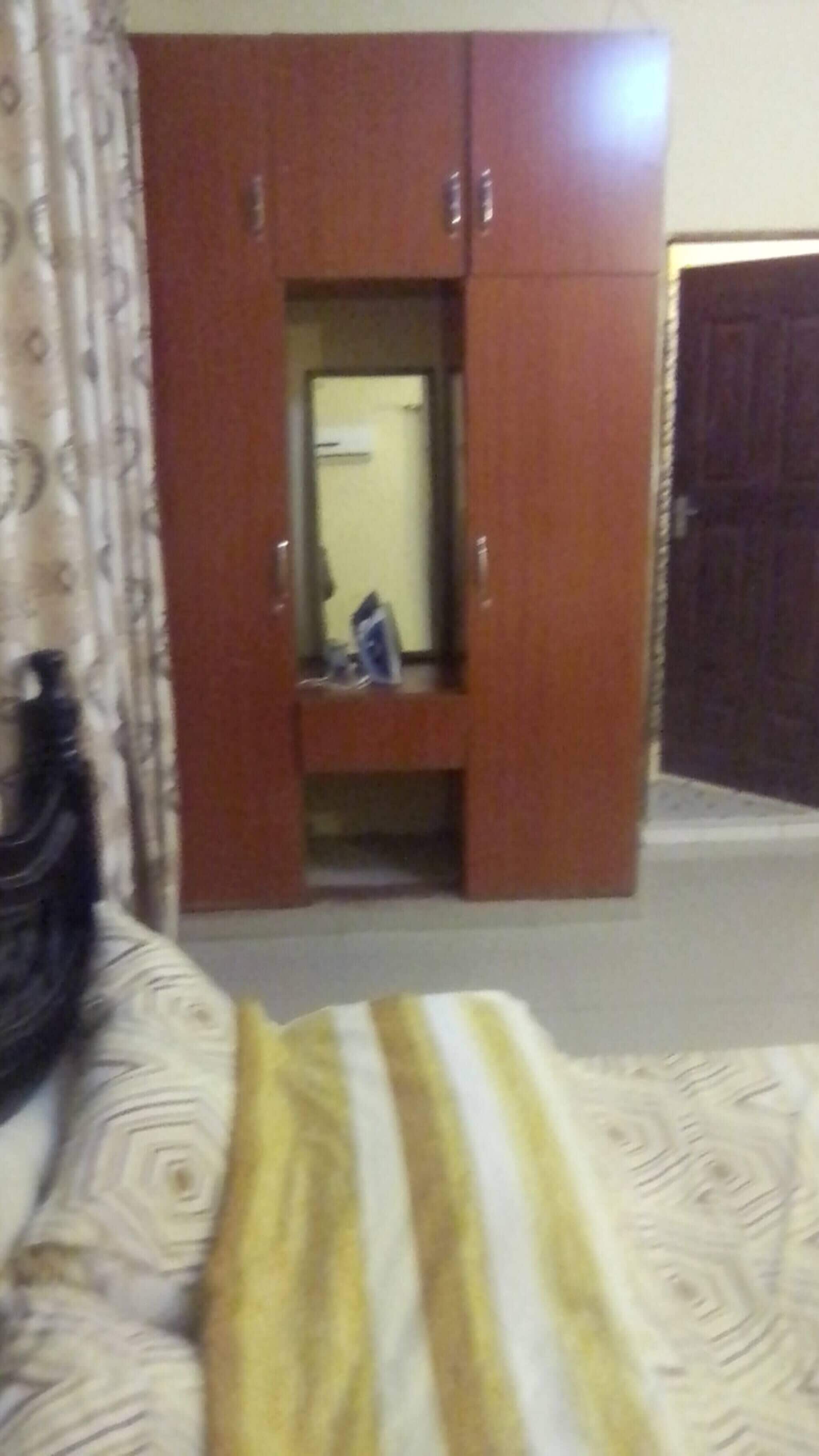 A room with a wardrobe, a bed with a patterned bedspread, and a door leading to another room.