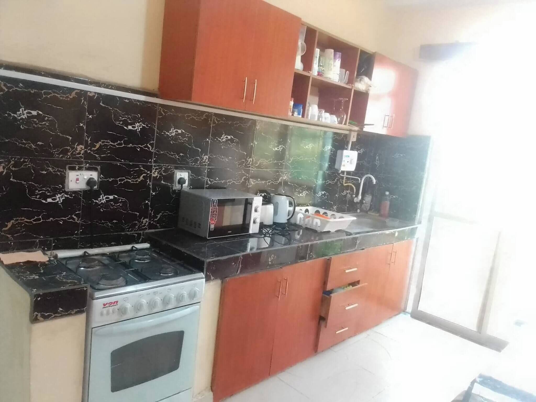 A kitchen with a gas stove, microwave, and a sink. There are cabinets above the counter and a window on the right.