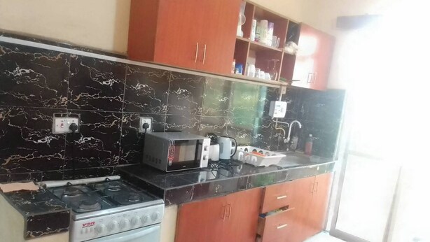 A kitchen with a gas stove, microwave, and a sink. There are cabinets above the counter and a window on the right. - Furnished Flat Apartment Bamburi Beach Mombasa (Mombasa)
