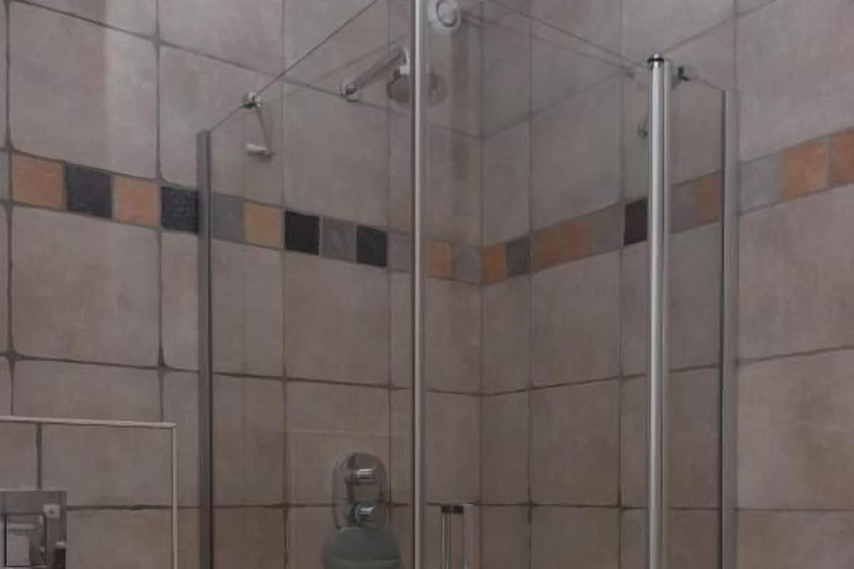 A shower with a glass door, tiled walls, and a toilet.