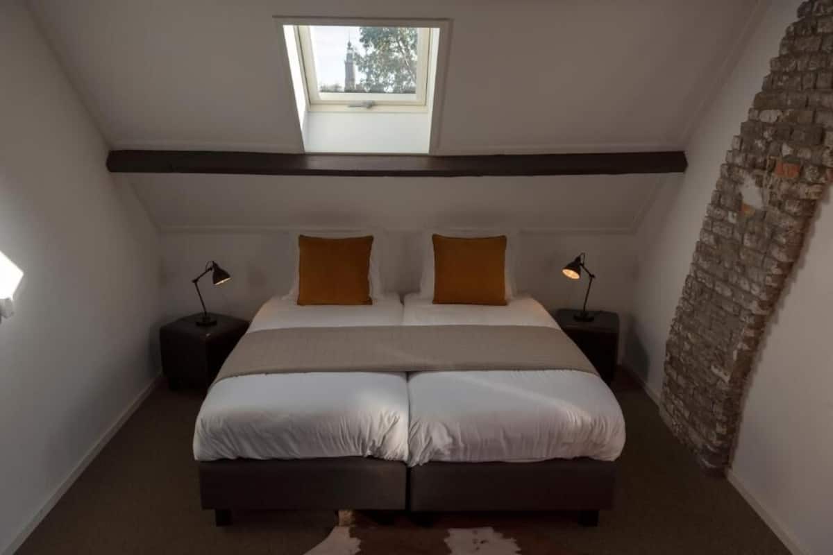 A bedroom with a skylight, a bed with two pillows, and a stone wall.