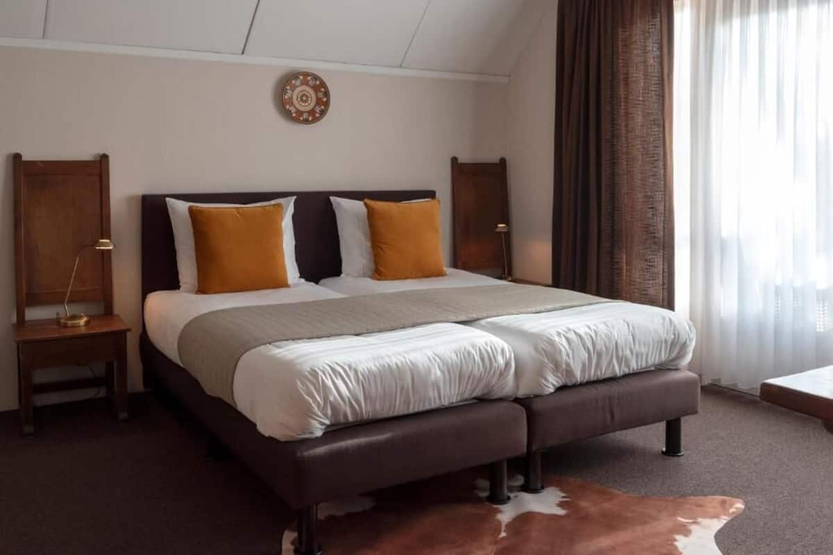 A double bed with a dark headboard, two nightstands, a cowhide rug, and a decorative plate on the wall.