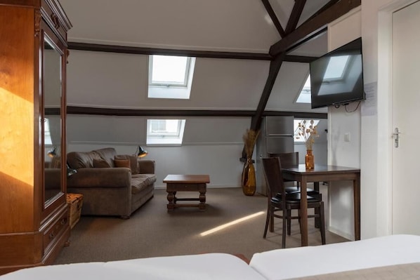 A room with a loft bed, a sofa, a dining table, and a TV mounted on the wall. - hcrslandswelvaren (Aardenburg)