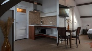 A compact kitchen with a microwave, a dining area with two chairs, a flat-screen TV mounted above the counter, and a door leading to another room. - hcrslandswelvaren (Aardenburg)