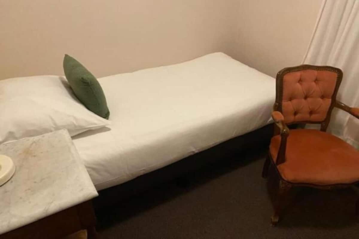 A small, single-bed room with a green pillow, a wooden chair, and a small table with a white surface.