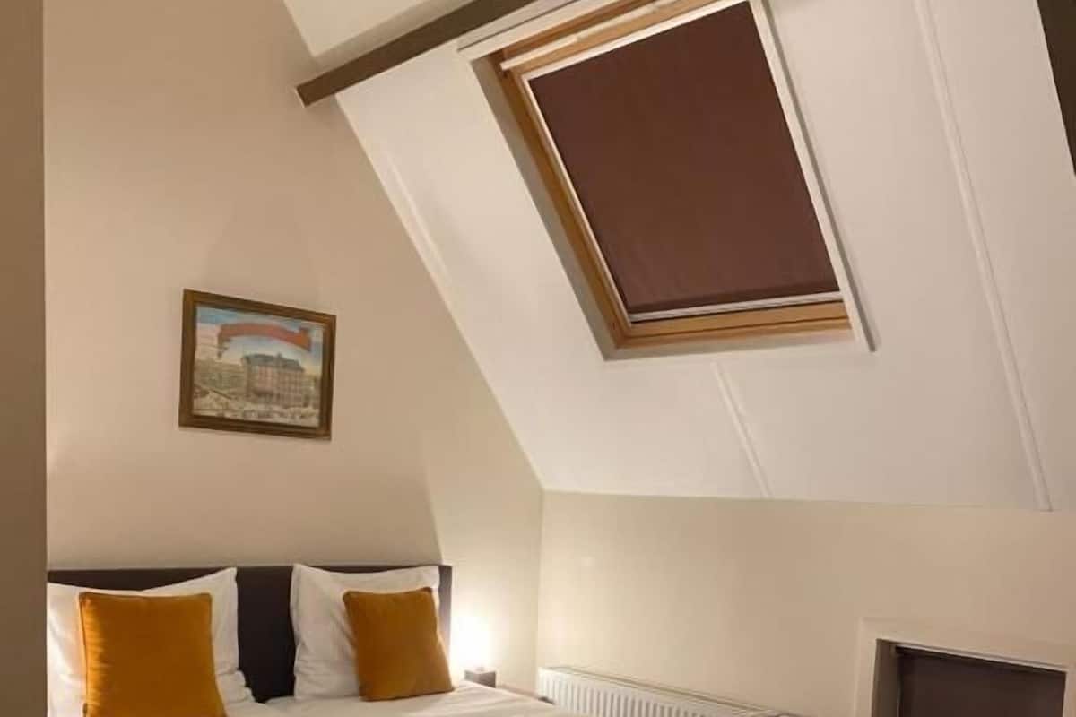 A bedroom with a bed, a radiator, a window, and a painting on the wall.