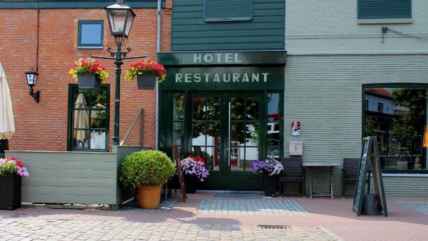 A hotel restaurant with a green facade, outdoor seating, and flower pots. - hcrslandswelvaren (Aardenburg)