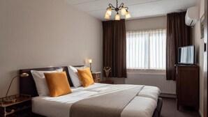 A hotel room with a large bed, a nightstand, a lamp, a television, and a window with curtains. - hcrslandswelvaren (Aardenburg)