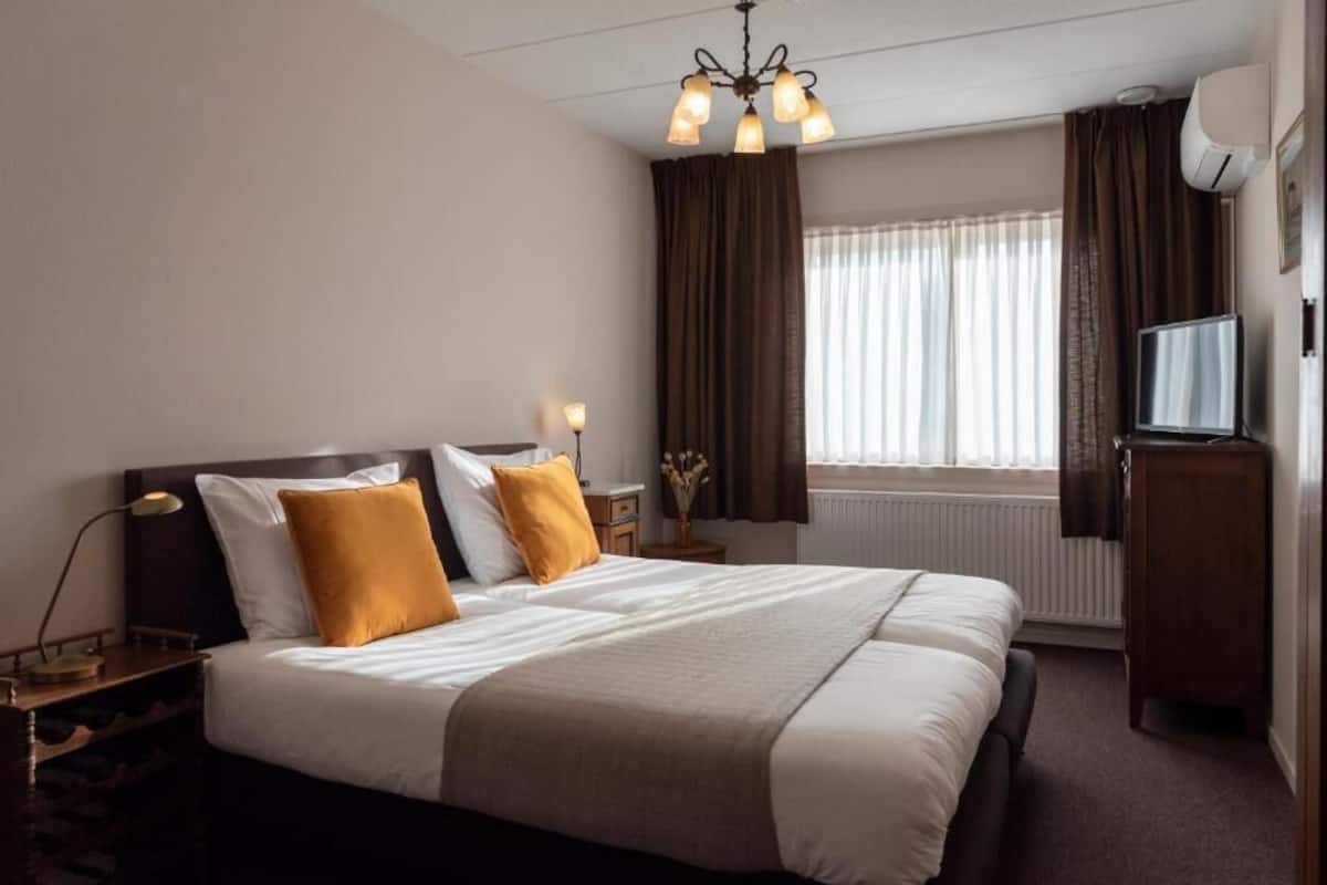 A hotel room with a large bed, a nightstand, a lamp, a television, and a window with curtains.