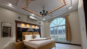 Une chambre moderne avec un grand lit, une table de chevet, un miroir et une grande fenêtre avec des rideaux.