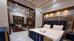 Une chambre moderne dotée d’un grand lit, d’un coin salon avec un canapé et des fauteuils, et d’un mur décoratif orné d’un motif évoquant le marbre.