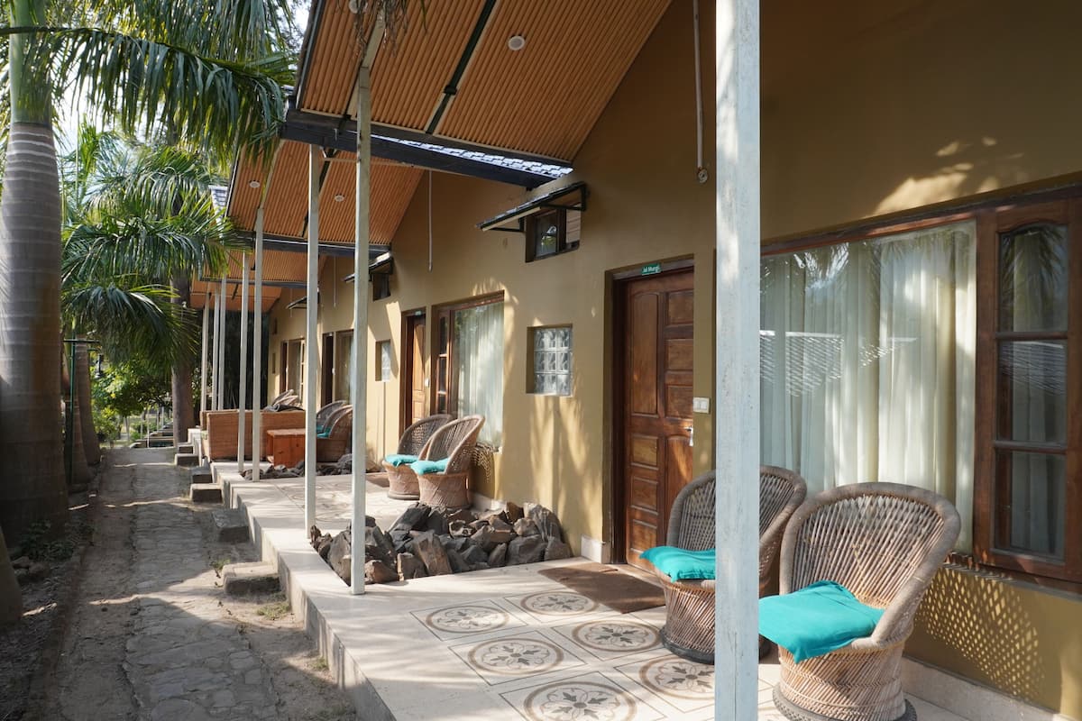 A covered outdoor seating area with wicker chairs and a stone pathway.