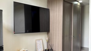 A modern, compact room with a built-in desk, a mounted TV, a wardrobe, and a trash bin. - Olive Athena Guesthouse (Denpasar)