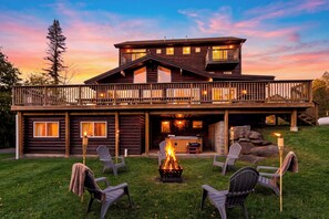 Eine zweistöckige Holzhütte mit einer Terrasse, Sitzgelegenheiten im Freien und einem Feuerkorb.