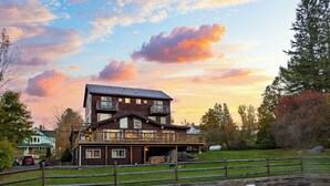 Eine zweistöckige Holzhütte mit einem Balkon, einem Schwimmbecken mit Liegestühlen und wolkenlosem Himmel.