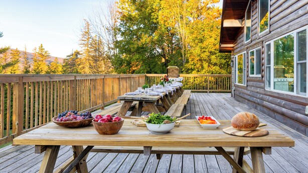 Eine Holzdar Terrasse mit Picknicktisch, umgeben von Bäumen und einer Holzhütte.
